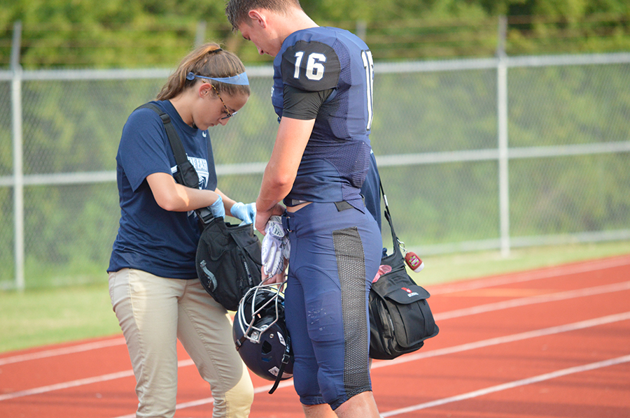 On and off // Junior Kelsey Pierce helps out football player Zachary Young on the sidelines during a Frisco Scrimmage Game. Photo by Whitney Tobias.