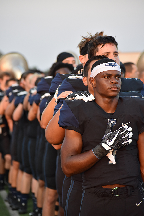With hand over heart, junior Corbin Johnson leads the football team in the lineup for the National Anthem against Rockwall Heath Sept. 1. No varsity player has taken a knee during the National Anthem.