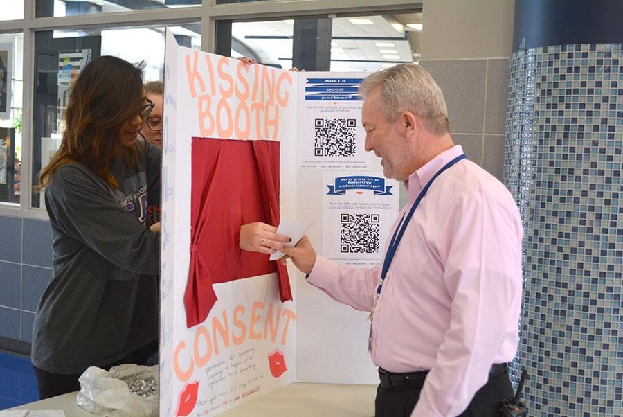 Counseling consent \ Giving a kiss, junior Amanda Kounlavouth hands Principal Mike Williams a Hersheys Kiss along with information addressing the importance for asking for consent to establish healthy boundaries in relationships in honor of National Teen Dating Violence Awareness Month. Student Council hosted the consent kissing booth during lunches Feb. 18. 