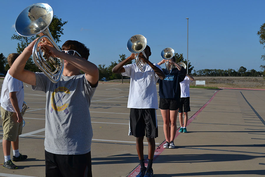 Melodic mellos// Rehearsing marching fundamentals, junior Blake Taber adjusts his mellophone horn angle to the sky while playing the opener for the 2017-2018 marching show “Through the Night”. Photo by Liz Harkins