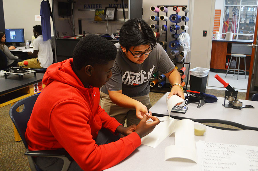 Spirit shop scholars // Cutting out vinyls for t-shirts, students Quincy Jackson and Miguel Vargas work on Spirit Shop products and focus on small details. Students work while managers make future plans about the Spirit Shop with teacher Mr. Hood. 
