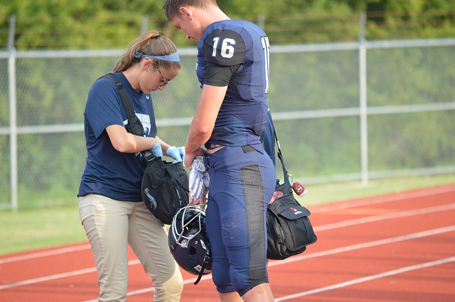 On and off // Junior Kelsey Pierce helps out football player Zachary Young on the sidelines during a Frisco Scrimmage Game. Photo by Whitney Tobias.