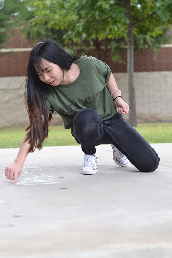 Walk the chalk // Writing happy messages, sophomore Huong Huynh prepares for the first Wylie Way day of the year. Student council members volunteered to write inspiring messages in chalk by each school entrance.