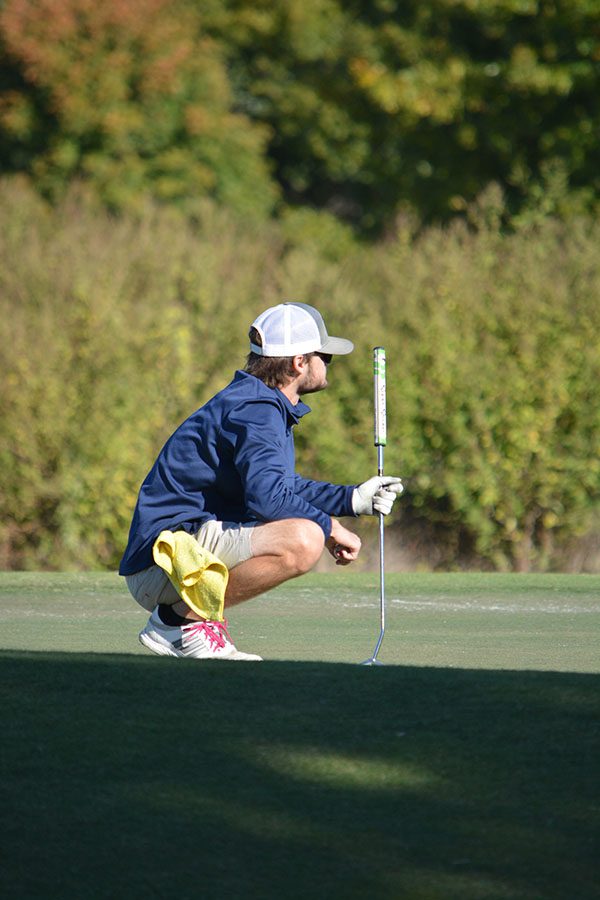 Size up // Examining the green, senior Ethan Travis inspects the ground for dips and other obstacles before putting.  