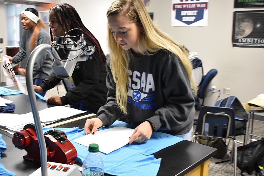 Lining it up // Centering the logo, senior Destini Cole places the shirt under a laser aligner, to place the design precisely on the shirt to make sure it’s not crooked, and aligned with the other shirts.
