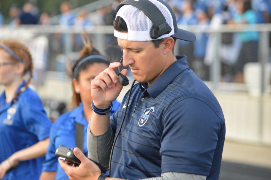 In the mode // Looking at his radio, Varsity Wide Receiver Coach Garrett Horvath prepares for his first pre-season game of the season against Mount Pleasant Oct.31. Varsity lost 56-42. Coach Horvath came here from Denton High School this year.